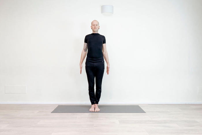 A person at a standing desk taking a short stretch break, reaching arms upward in a naturally lit office space